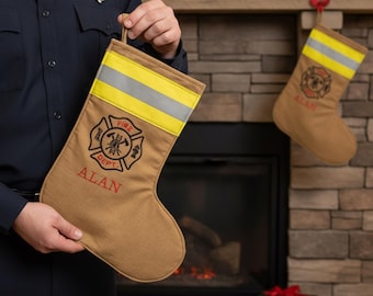 May include: Tan Christmas stocking with a yellow and reflective silver stripe, and the words "FIRE DEPT" and "ALAN" embroidered in red. The stocking features a fire department emblem. Another stocking hangs in the background.