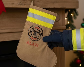 May include: Tan Christmas stocking with a yellow and silver reflective stripe, the words "FIRE DEPT" and a fire department emblem, and the name "ALAN" embroidered in red. The stocking is held by a person wearing a firefighter's uniform.