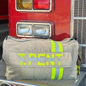 May include: A large, beige duffel bag with a black zipper and a yellow reflective stripe. The bag has the text "T. PENT" embroidered on the front in yellow.