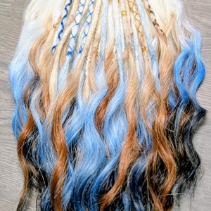 May include: A collection of handmade dreadlocks in a variety of colors. The dreadlocks feature a gradient effect, transitioning from blonde to brown, blue, and black. Some dreadlocks are adorned with blue and gold accents.