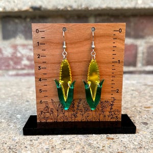 May include: A pair of yellow and green corn cob earrings on a wooden display stand with a ruler. The earrings are about 2 inches long.