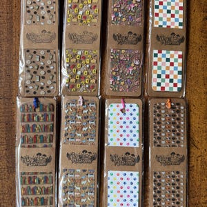 May include: A collection of ten bookmarks with various designs, including coffee cups, numbers, mushrooms, checkered patterns, bookshelves, dogs, paw prints, and cat faces. Each bookmark is packaged in a clear plastic sleeve and has a decorative top.