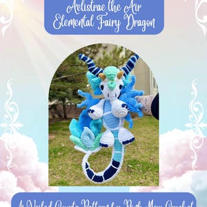 May include: A handmade crochet dragon in shades of white, blue, and teal. The dragon has large wings, horns, and a long tail. The text "Aelistrae the Air Elemental Fairy Dragon" and "A Veiled Courts Pattern by Pink Mew Crochet" are displayed.