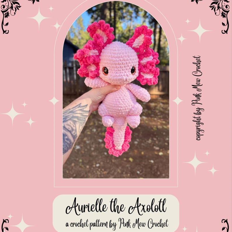 Puede incluir: Un juguete de peluche axolotl de crochet rosa con volantes rosas alrededor de la cabeza y la cola. El juguete est&aacute; siendo sostenido por una mano con un tatuaje. El texto "Aurielle the Axolotl" y "a crochet pattern by Pink Mew Crochet" est&aacute; en la parte inferior de la imagen.