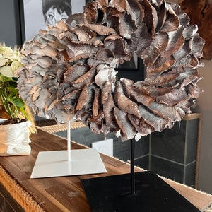 Könnte beinhalten: Zwei dekorative Kränze aus getrockneten Pilzen, einer mit einem weißen Sockel und der andere mit einem schwarzen Sockel. Die Kränze werden auf einer Holzoberfläche präsentiert.