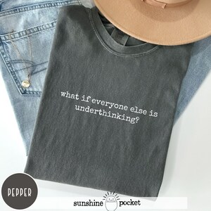 Peut inclure: Un t-shirt &agrave; col rond gris anthracite avec le texte blanc "what if everyone else is underthinking?" imprim&eacute; sur le devant. Le v&ecirc;tement pr&eacute;sente une coupe standard &agrave; manches courtes, affichant un style d&eacute;contract&eacute; avec une police claire.