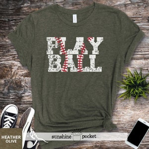 May include: A green t-shirt with the words "PLAY BALL" printed on it in white with a red baseball graphic. The shirt has a distressed look.