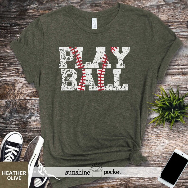 May include: A green t-shirt with the words "PLAY BALL" printed on it in white with a red baseball graphic. The shirt has a distressed look.