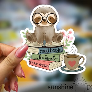 May include: A sticker featuring a cartoon sloth wearing glasses and sitting on a stack of books. The books have the text "read books be kind stay weird". There is a cup of coffee with steam coming from it next to the books.