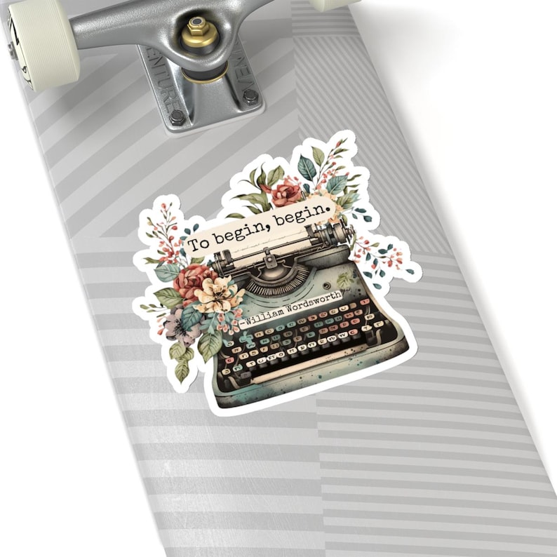 K&ouml;nnte beinhalten: Eine Vintage-Schreibmaschine mit floralen Akzenten und dem Zitat "Um zu beginnen, beginne." von William Wordsworth.