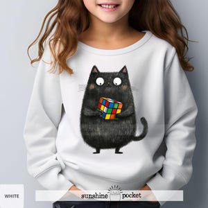 May include: White sweatshirt with a black cat holding a colorful Rubik's Cube. The cat has a playful expression and is wearing a white sweatshirt with the words "sunshine pocket" on the bottom.