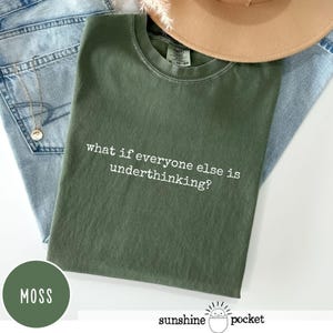 Peut inclure: Un t-shirt &agrave; col rond vert mousse avec le texte blanc "what if everyone else is underthinking?" imprim&eacute; sur la poitrine. Le t-shirt pr&eacute;sente une coupe standard avec un col c&ocirc;tel&eacute; et est pos&eacute; &agrave; plat sur un tissu en jean bleu clair.