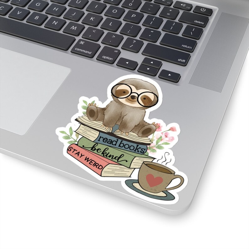 May include: A sticker featuring a cartoon sloth wearing glasses and sitting on a stack of books. The books have the text "read books be kind" and "STAY WEIRD". There is a cup of coffee with a heart on it next to the sloth.