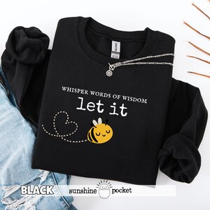 May include: Black sweatshirt with the text "Whisper words of wisdom, let it" and a cartoon bee graphic. The bee is yellow and black. A silver necklace is draped across the sweatshirt. The words "BLACK sunshine pocket" are at the bottom.