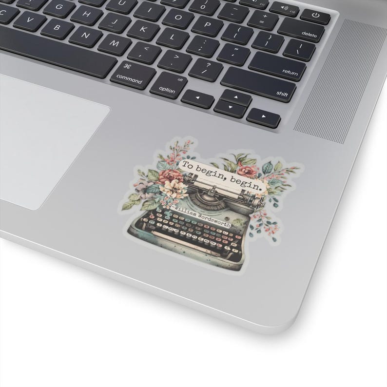 K&ouml;nnte beinhalten: Eine Vintage-Schreibmaschine mit floralen Akzenten und dem Zitat "Um zu beginnen, beginne." von William Wordsworth.