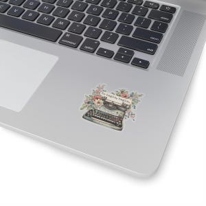 K&ouml;nnte beinhalten: Eine Vintage-Schreibmaschine mit floralen Akzenten und dem Text "To begin, begin." Die Schreibmaschine ist blau und schwarz mit einer wei&szlig;en Tastatur. Die Blumen sind rosa, wei&szlig; und gelb.