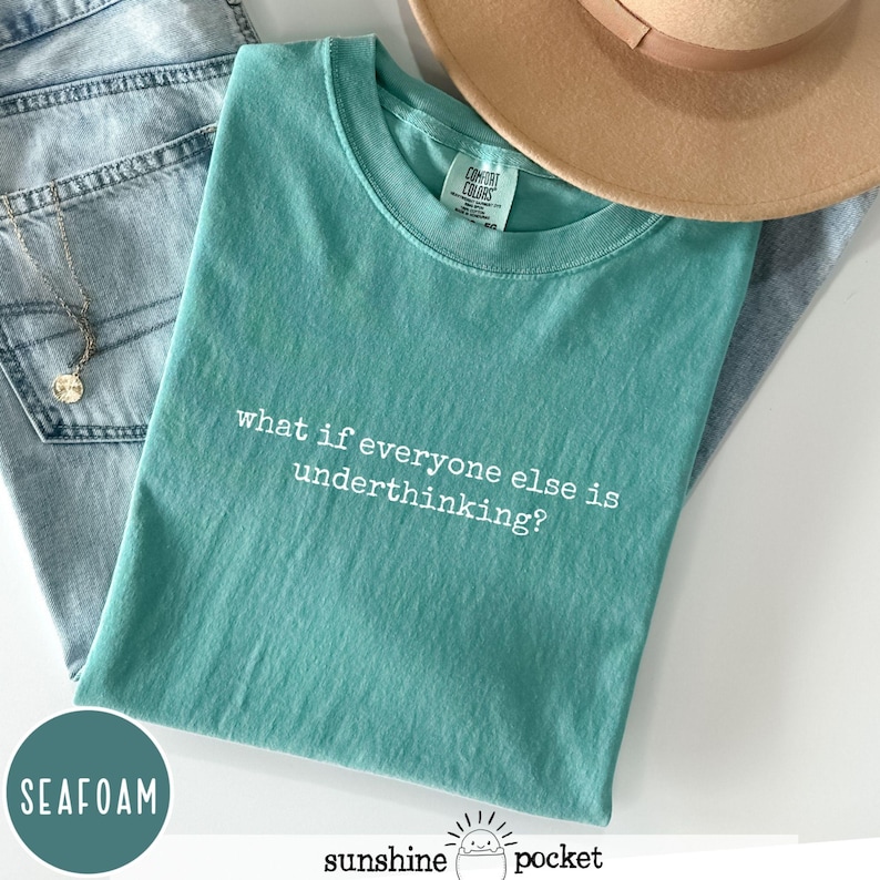 Peut inclure: Un t-shirt &agrave; manches courtes vert mousse avec le texte imprim&eacute; en blanc "what if everyone else is underthinking?" sur la poitrine. Le t-shirt pr&eacute;sente une encolure ronde et une &eacute;tiquette de marque Comfort Colors visible &agrave; l'int&eacute;rieur du col.