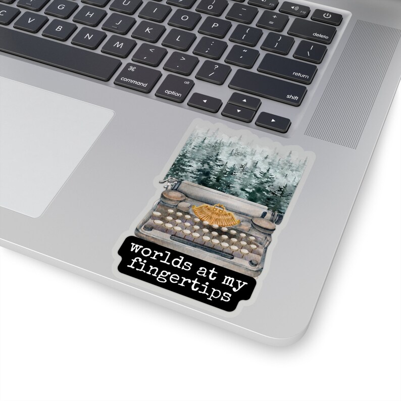 May include: A vintage typewriter with a gold key and a forest scene behind it. The text "worlds at my fingertips" is printed on a black rectangle below the typewriter.