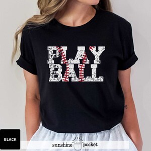May include: Black t-shirt with a white distressed graphic that says "PLAY BALL" with a red baseball graphic in the middle of the word "PLAY".