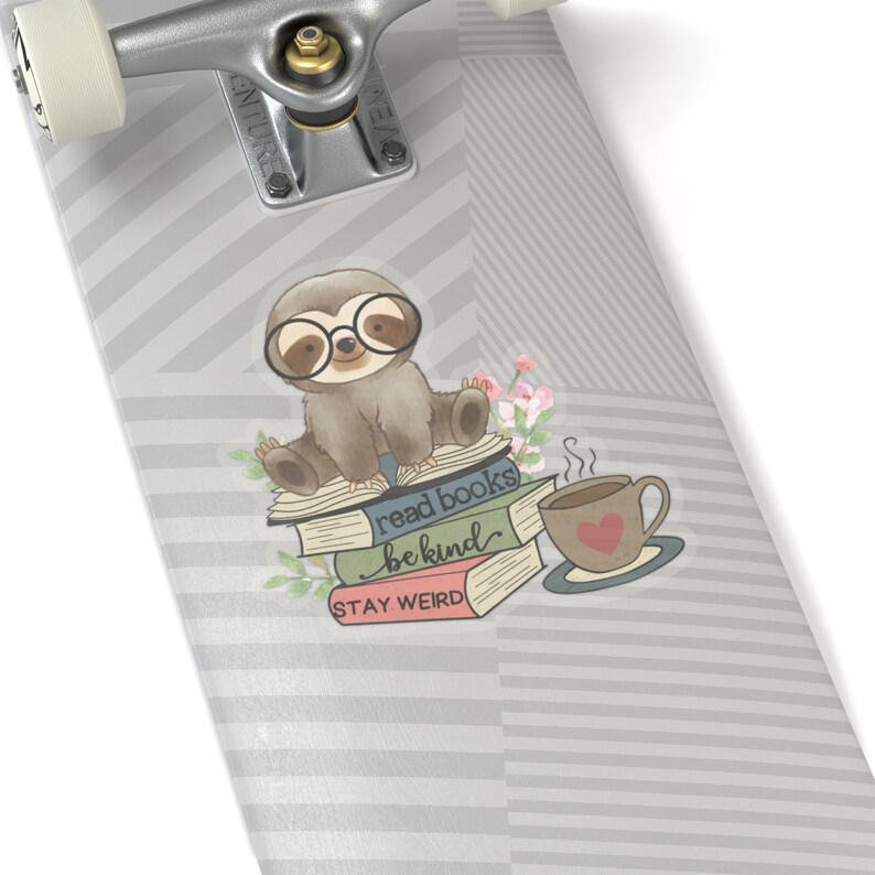 May include: A gray and white striped skateboard with a sticker of a sloth wearing glasses and sitting on a stack of books. The books have the text "read books be kind stay weird". There is a cup of coffee with steam coming from it.