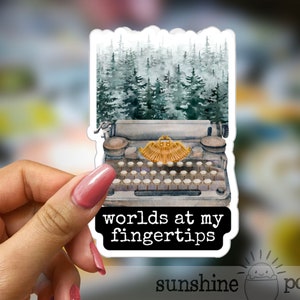 May include: A vintage typewriter with a forest scene behind it. The typewriter has a gold-colored carriage return lever and the text "worlds at my fingertips" is printed below it.