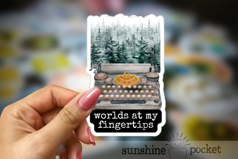 May include: A vintage typewriter with a forest scene behind it. The typewriter has a gold-colored carriage return lever and the text "worlds at my fingertips" is printed below it.