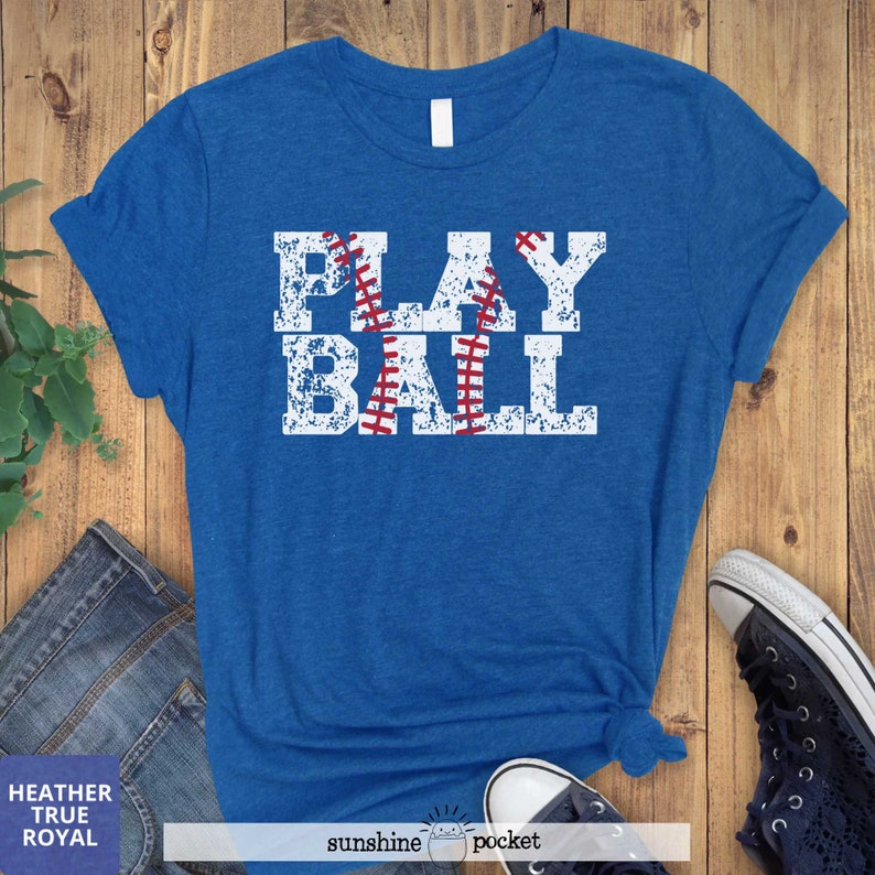 May include: A blue t-shirt with a white distressed graphic that says "PLAY BALL" with a baseball graphic in the middle of the word "PLAY".