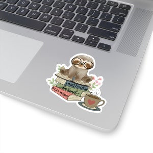 May include: A sticker featuring a cartoon sloth wearing glasses and sitting on a stack of books. The books have the text "read books be kind" and "STAY WEIRD". There is a cup of coffee with a heart on it next to the sloth.