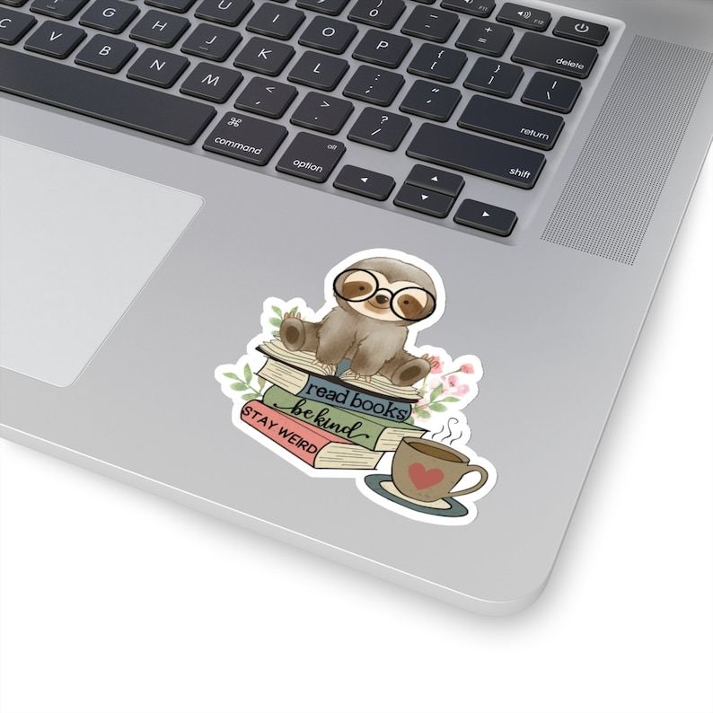 May include: A sticker featuring a cartoon sloth wearing glasses and sitting on a stack of books. The books have the text "read books be kind" and "STAY WEIRD". There is a cup of coffee with a heart on it next to the sloth.