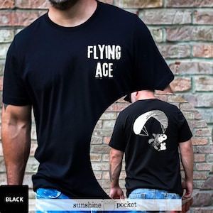 May include: Black t-shirt with the text "FLYING ACE" in white block letters. The back of the shirt features a cartoon illustration of a character paragliding. The bottom of the shirt has the text "sunshine pocket".