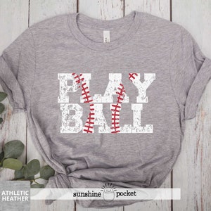 May include: Gray t-shirt with a white distressed graphic that says "PLAY BALL" with a red baseball graphic in the middle of the word "BALL".