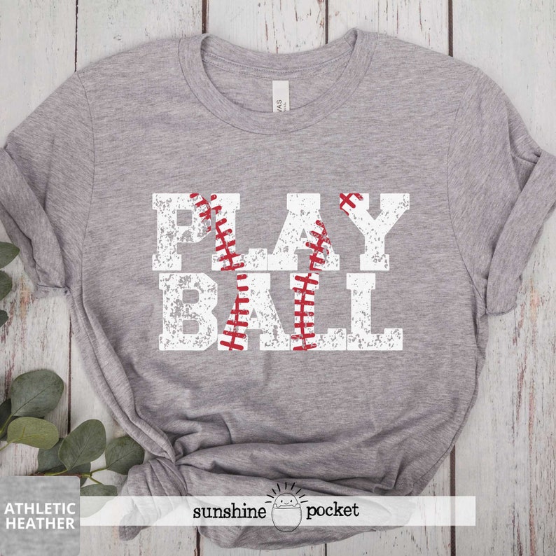 May include: Gray t-shirt with a white distressed graphic that says "PLAY BALL" with a red baseball graphic in the middle of the word "BALL".