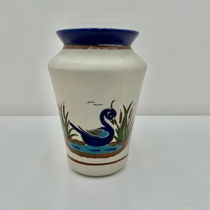 May include: A white ceramic vase with a blue rim and a painted design of a blue bird in a pond with green reeds.