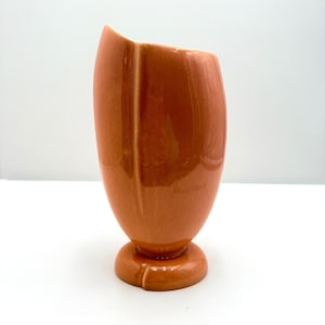 May include: A tall, orange ceramic vase with a glossy finish. The vase has a unique, curved shape with a wide opening and a rounded base. The vase is approximately 8 inches tall.
