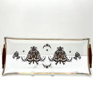 May include: Rectangular glass serving tray with gold trim and wooden handles. The tray features a white background with a repeating dot pattern and decorative brown and gold floral and bird designs. A vintage serving piece.