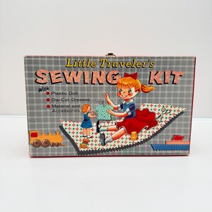May include: A vintage Little Traveler's Sewing Kit box with a cartoon illustration of a girl sewing. The box is gray with a red and white checkered pattern and features the text "Little Traveler's SEWING KIT". Includes a plastic doll, die-cut dresses, and accessories.