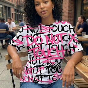 Female model wearing edgy all-over “Do Not Touch” graffiti typography t-shirt design in black and hot pink streetwear style