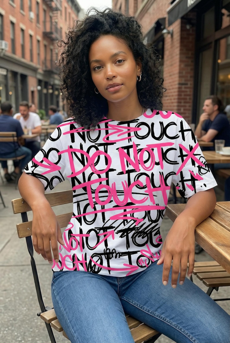 Female model wearing edgy all-over “Do Not Touch” graffiti typography t-shirt design in black and hot pink streetwear style