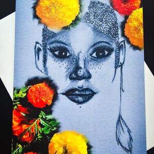 May include: A blue pencil portrait of a face, adorned with marigold flowers. The drawing features detailed eyes, lips, and freckles. The marigolds are yellow and orange, with green foliage. A single feather earring hangs from one ear.