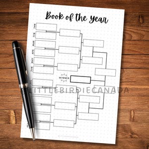 May include: A black pen rests on a white paper with a bracket-style chart labeled "Book of the year." The chart has boxes for entries and a "Winner" section. The paper is dotted and sits on a wooden surface.