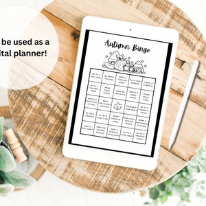 Puede incluir: Un planificador digital en una tableta con una ilustraci&oacute;n en blanco y negro de una tarjeta de bingo de oto&ntilde;o. La tarjeta tiene casillas con actividades como "Ir a una feria de oto&ntilde;o", "Hornear una tarta de manzana" y "Llevar un disfraz de Halloween".