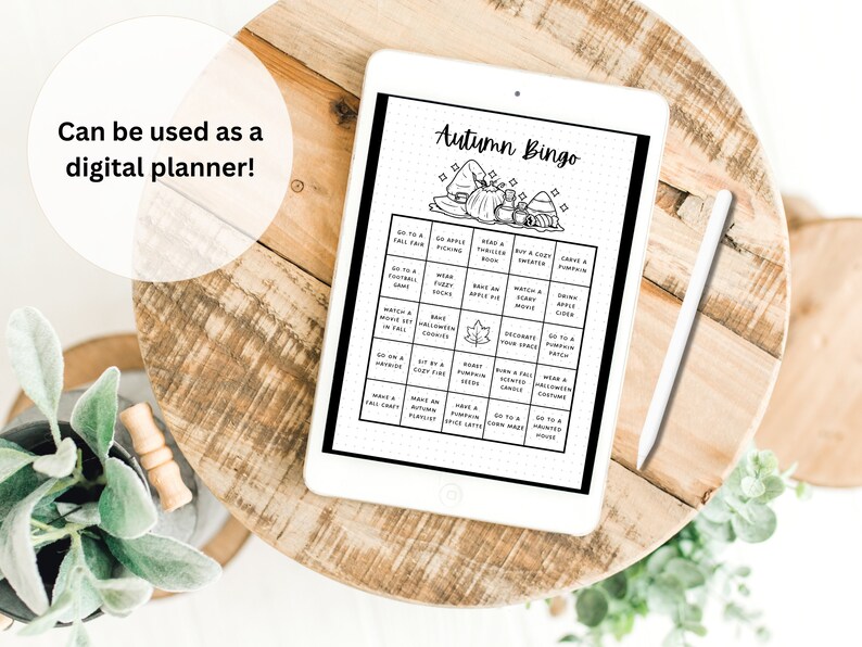 Puede incluir: Un planificador digital en una tableta con una ilustraci&oacute;n en blanco y negro de una tarjeta de bingo de oto&ntilde;o. La tarjeta tiene casillas con actividades como "Ir a una feria de oto&ntilde;o", "Hornear una tarta de manzana" y "Llevar un disfraz de Halloween".