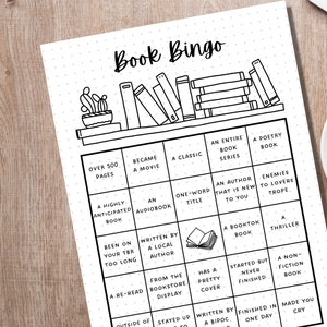 May include: Black and white Book Bingo game sheet with a bookshelf illustration at the top. The bingo card includes squares with prompts like "Over 500 Pages," "A Classic," and "A Thriller." A cup of coffee sits to the right.