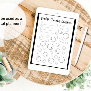 Puede incluir: Una tableta digital blanca con una pantalla negra que muestra un "Daily Shower Tracker" con un dise&ntilde;o de burbujas. La tableta est&aacute; sobre una mesa de madera con un l&aacute;piz blanco a su lado.