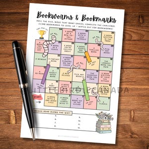 Op de afbeelding: Een geprint spelbord getiteld Bookworms & Bookmarks met een raster van genummerde vakjes met leesuitdagingen, ge&iuml;llustreerd met kleurrijke wormen, boekenleggers en een trofee, vergezeld door een zwarte balpen op een houten ondergrond.