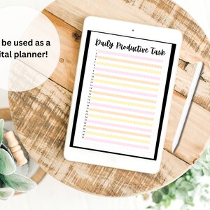 May include: A white tablet with a black border and a white stylus on a wooden table. The tablet screen displays a digital planner with the text "Daily Productive Task" and a list of numbered tasks.