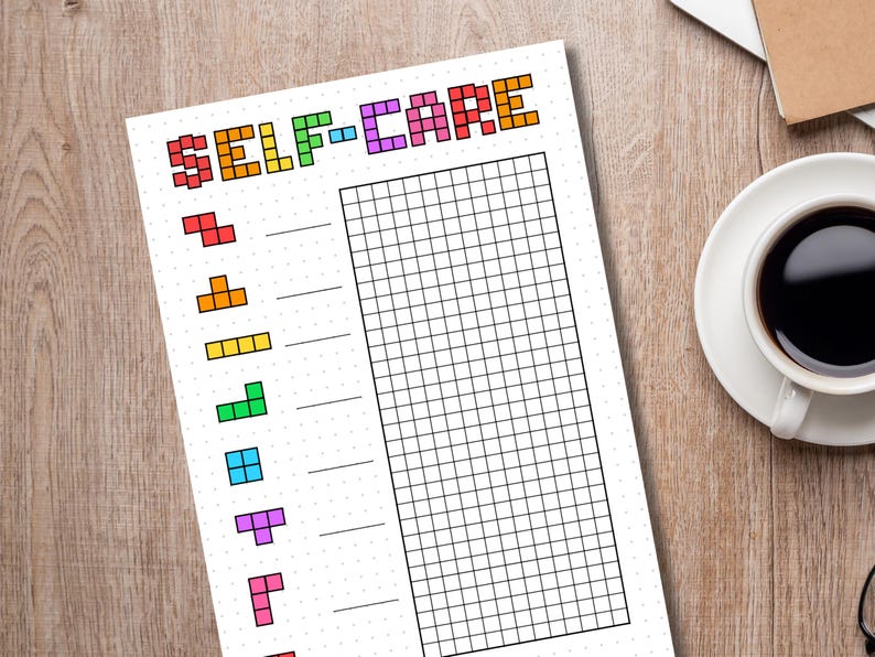 May include: A white self-care planner sheet with the words "SELF-CARE" in colorful pixelated letters. Below the title are colorful Tetris-like shapes. The sheet has a grid for tracking and is on a wooden surface.