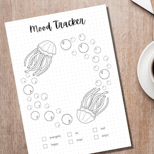 Może przedstawiać: Drukowany tracker nastroju z czarno-białą ilustracją dw&oacute;ch meduz otoczonych bąbelkami. Tracker zawiera listę nastroj&oacute;w: energiczny, szczęśliwy, ok, zmęczony, smutny i zły.