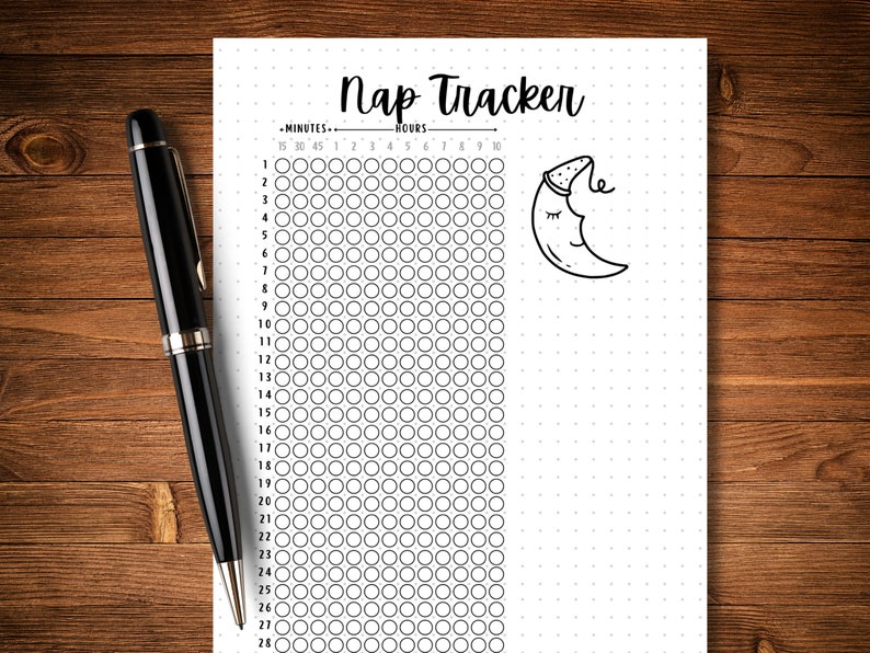 May include: A black pen rests on a white dotted paper with a "Nap Tracker" heading. The paper features a grid for tracking minutes and hours, with a crescent moon illustration wearing a nightcap. The background is a wooden surface.