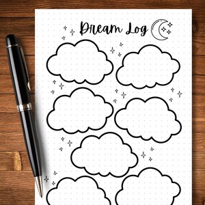 May include: A black pen rests beside a white Dream Log journal. The journal features cloud outlines for recording dreams, with the words "Dream Log" at the top, along with stars and a crescent moon.